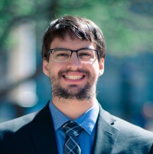 Seth Villegas smiles outside in the sun with blurred trees in the background